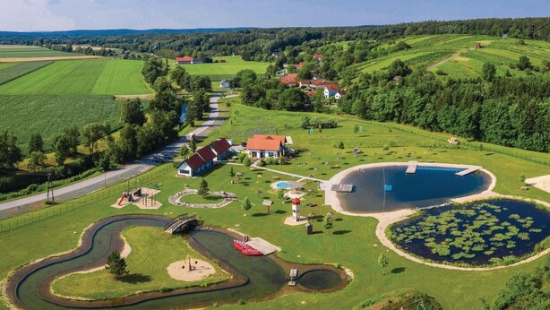 A rural landscape with a swimming pool, a winding path, and a small bridge.