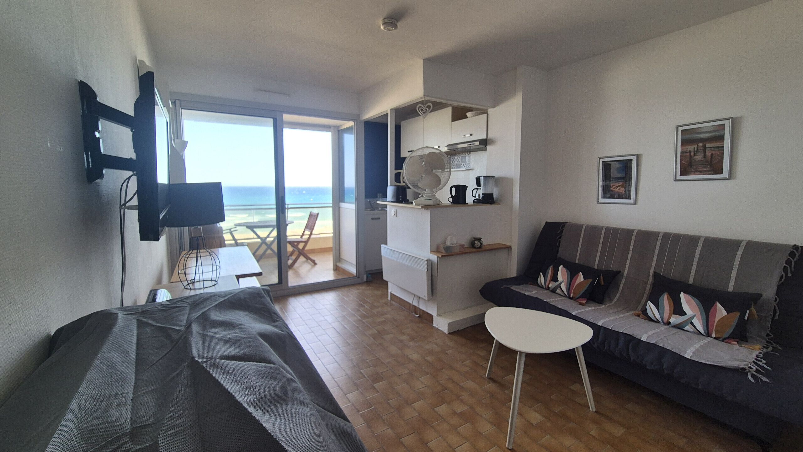 A living room with a sofa, a small table, a TV, and a balcony with a view.