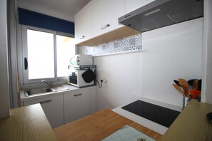 A compact kitchen with white cabinets, a wooden countertop, a microwave, and a window providing natural light.