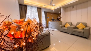 A hotel lobby with a reception desk, two grey sofas with yellow cushions, and a decorative plant arrangement. - Casa Retreat (Hulhumalé)