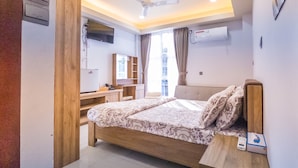 A modern bedroom with a bed, bedside table, and a desk with a chair. There is a TV mounted on the wall and an air conditioning unit. - Casa Retreat (Hulhumalé)