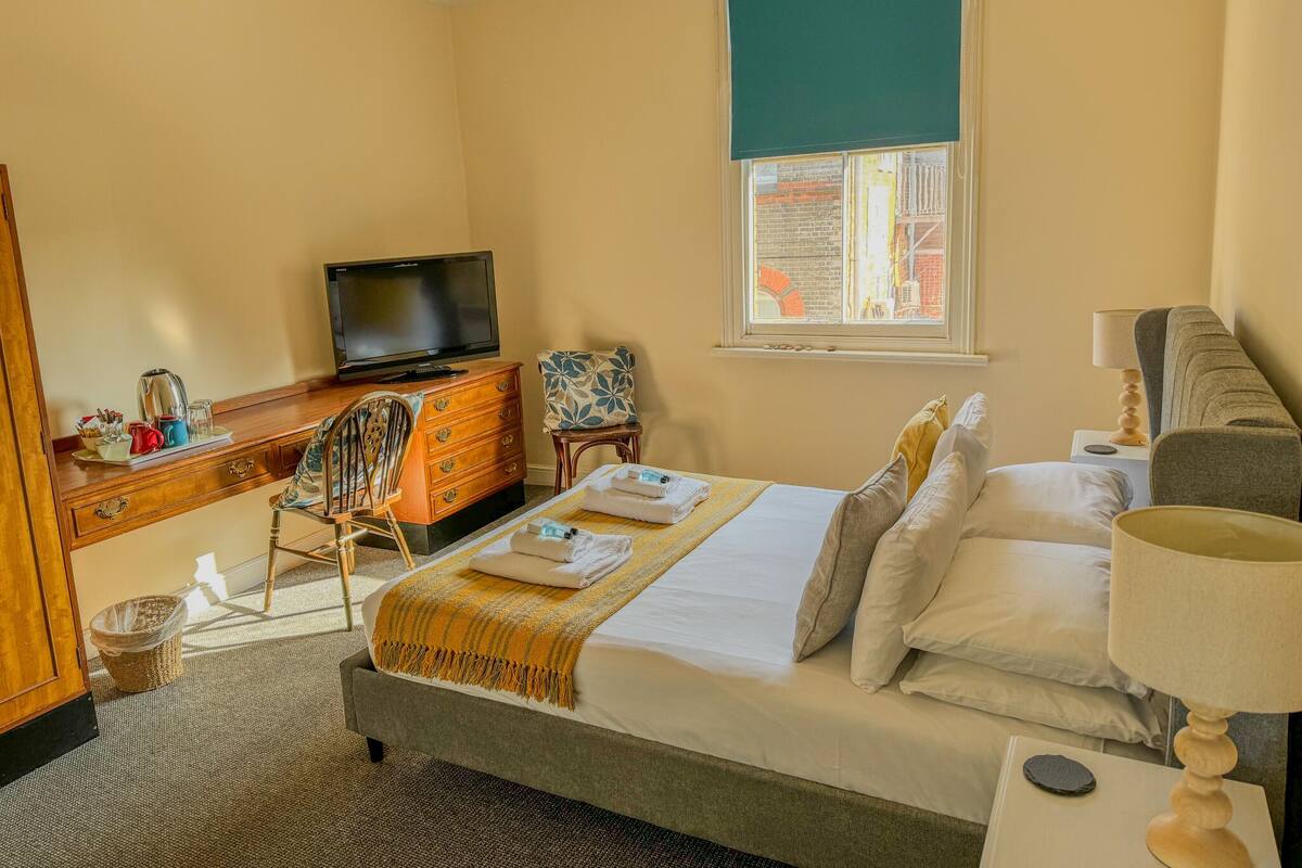 A hotel room with a bed, a television, a desk with a computer, a chair, and a window with a view of the outside.