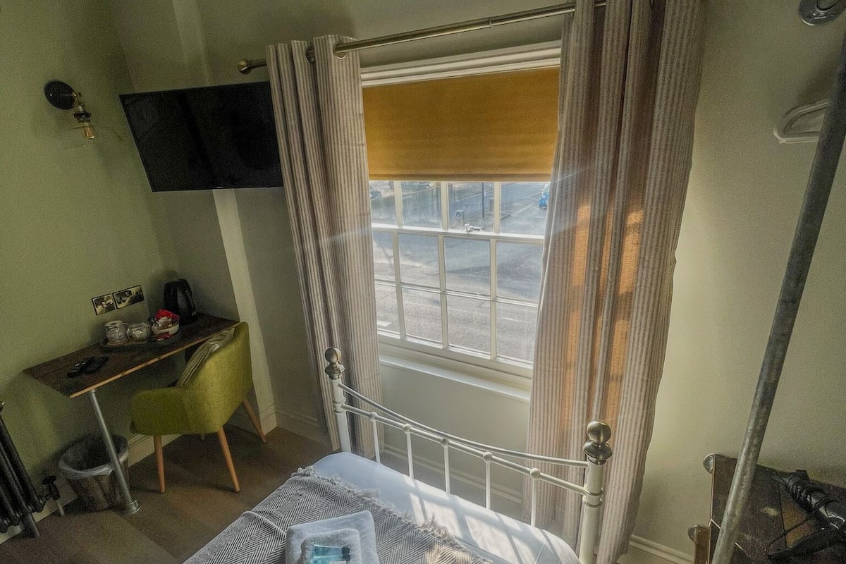 A hotel room with a bed, a desk, a chair, a television mounted on the wall, and a window with curtains.