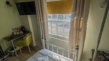 Ein Hotelzimmer mit einem Bett, einem Schreibtisch, einem Stuhl, einem an der Wand montierten Fernseher und einem Fenster mit Vorhängen.