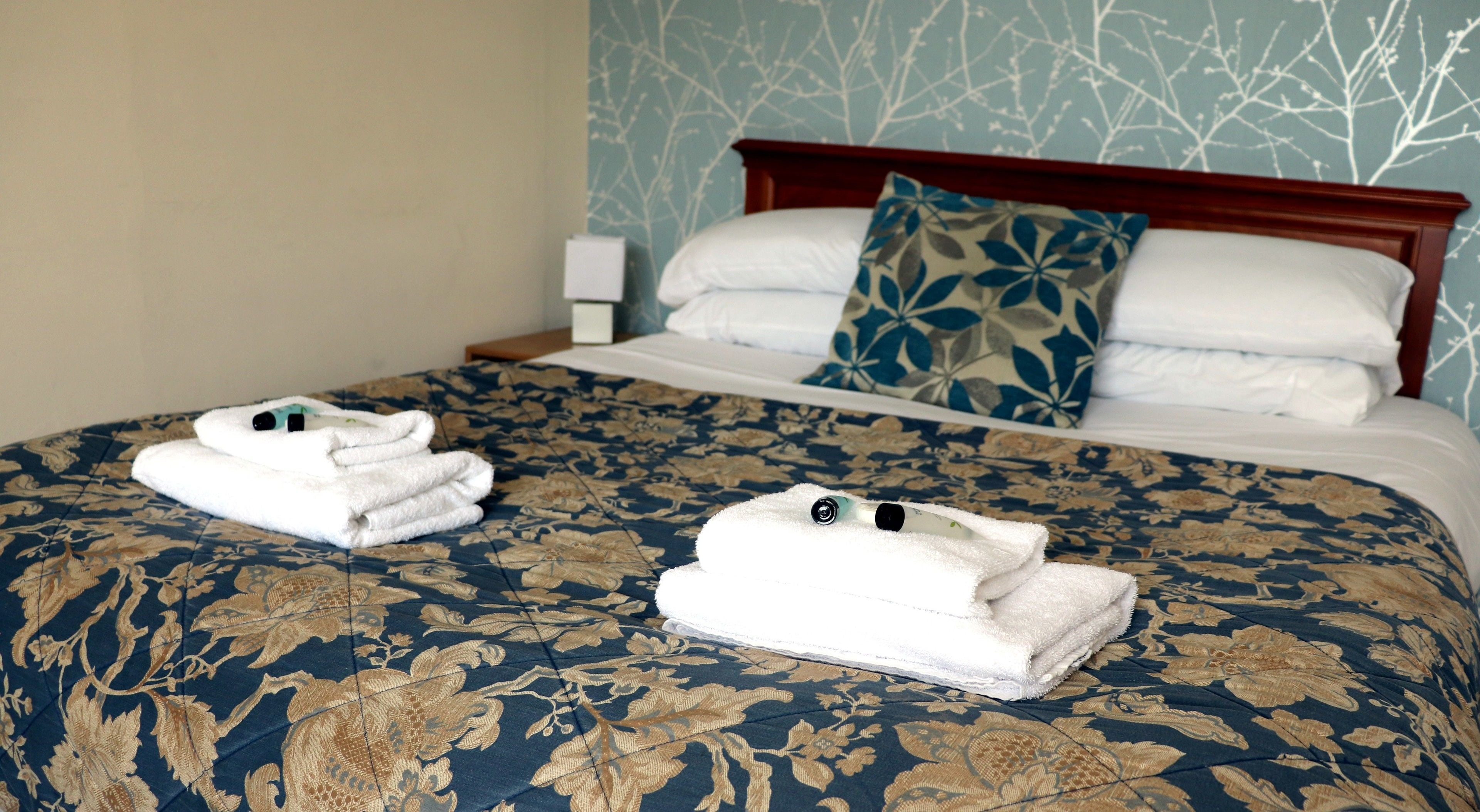 Ein ordentlich bezogenes Bett mit blumigem Muster, ein Holz-Kopfteil und eine blaue Wand mit Blatternmuster.