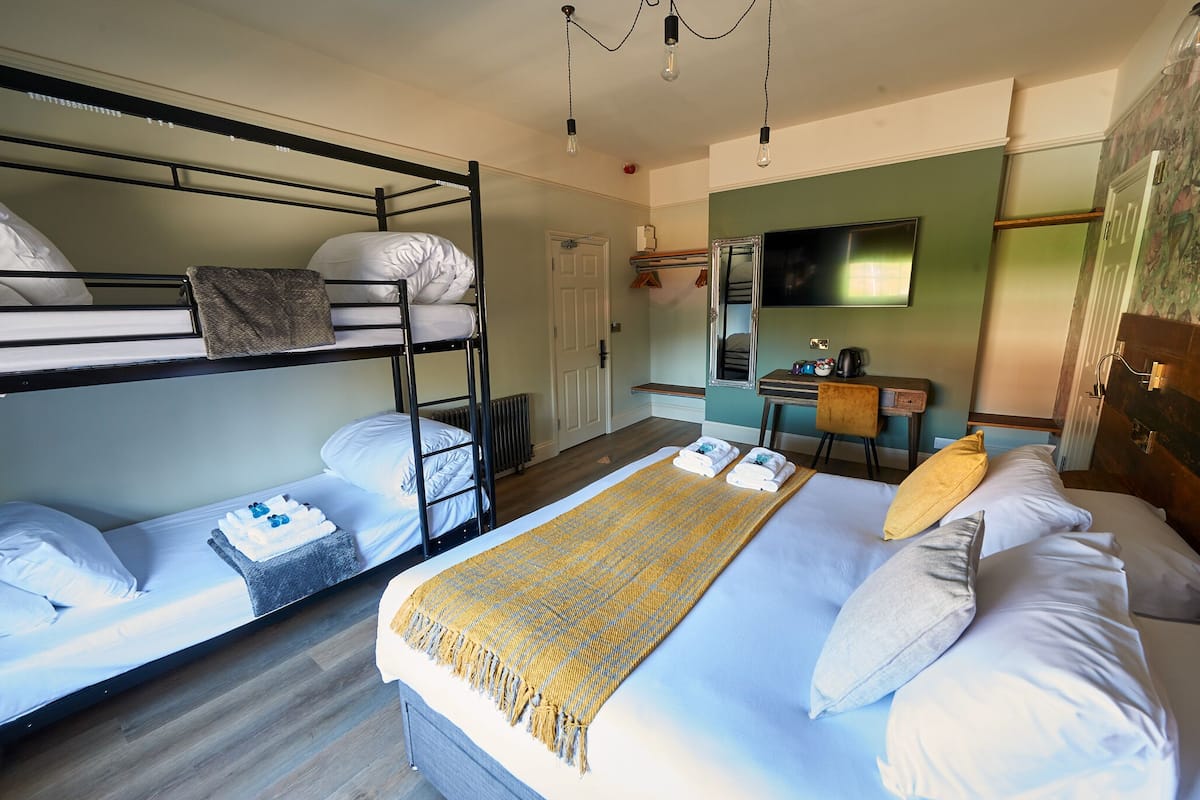 A room with bunk beds, a desk, a chair, and a bed with a blanket.