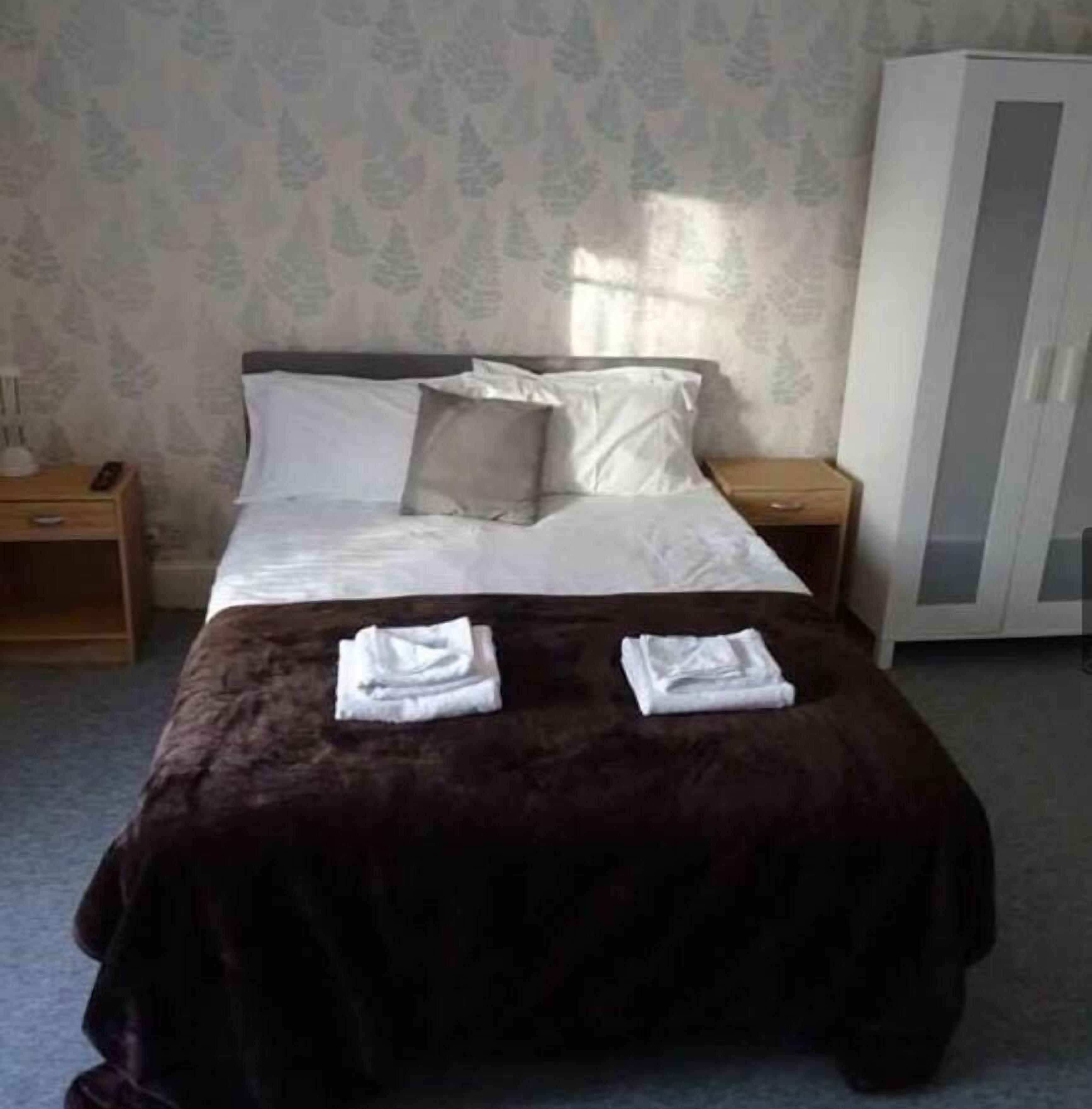 A neatly made bed with a dark brown bedspread and two folded towels on the foot of the bed.