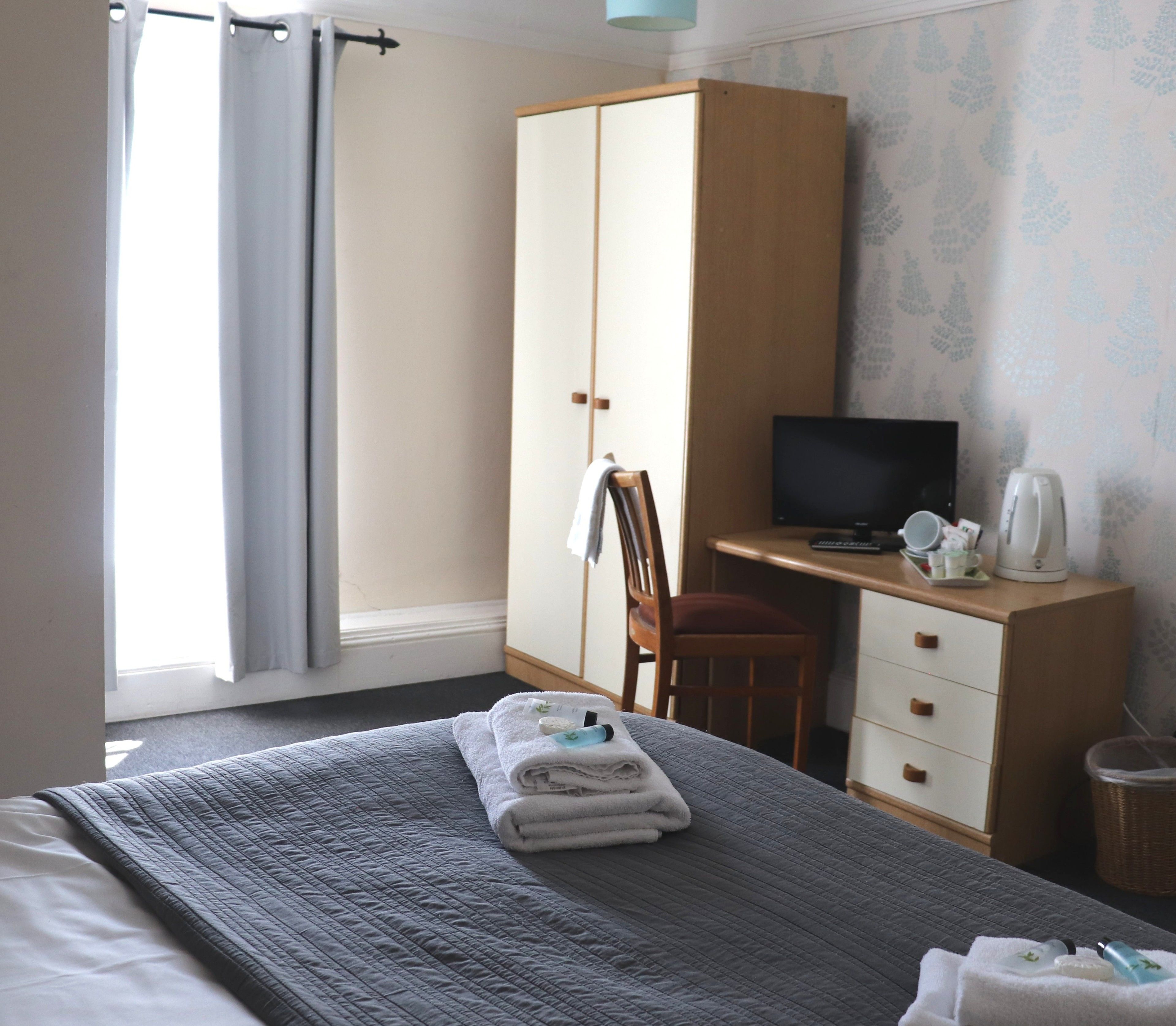 A hotel room with a bed, a desk, a chair, a television, and a wardrobe.