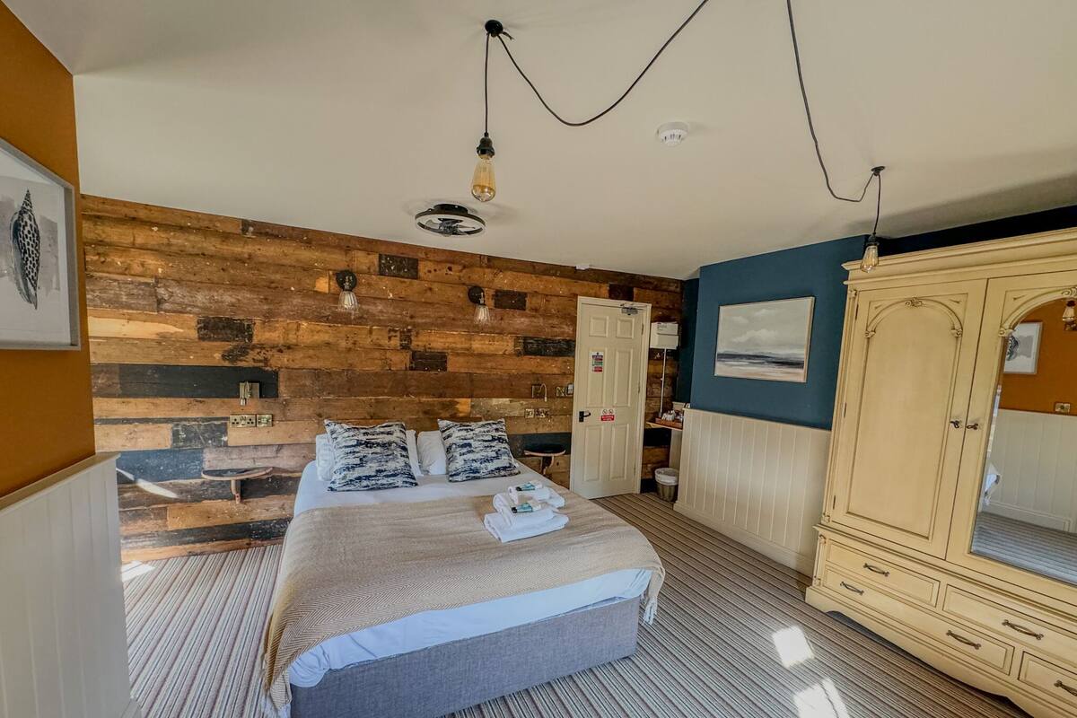 A bedroom with a wooden headboard, a bed with patterned pillows, a wardrobe, and a painting on the wall.