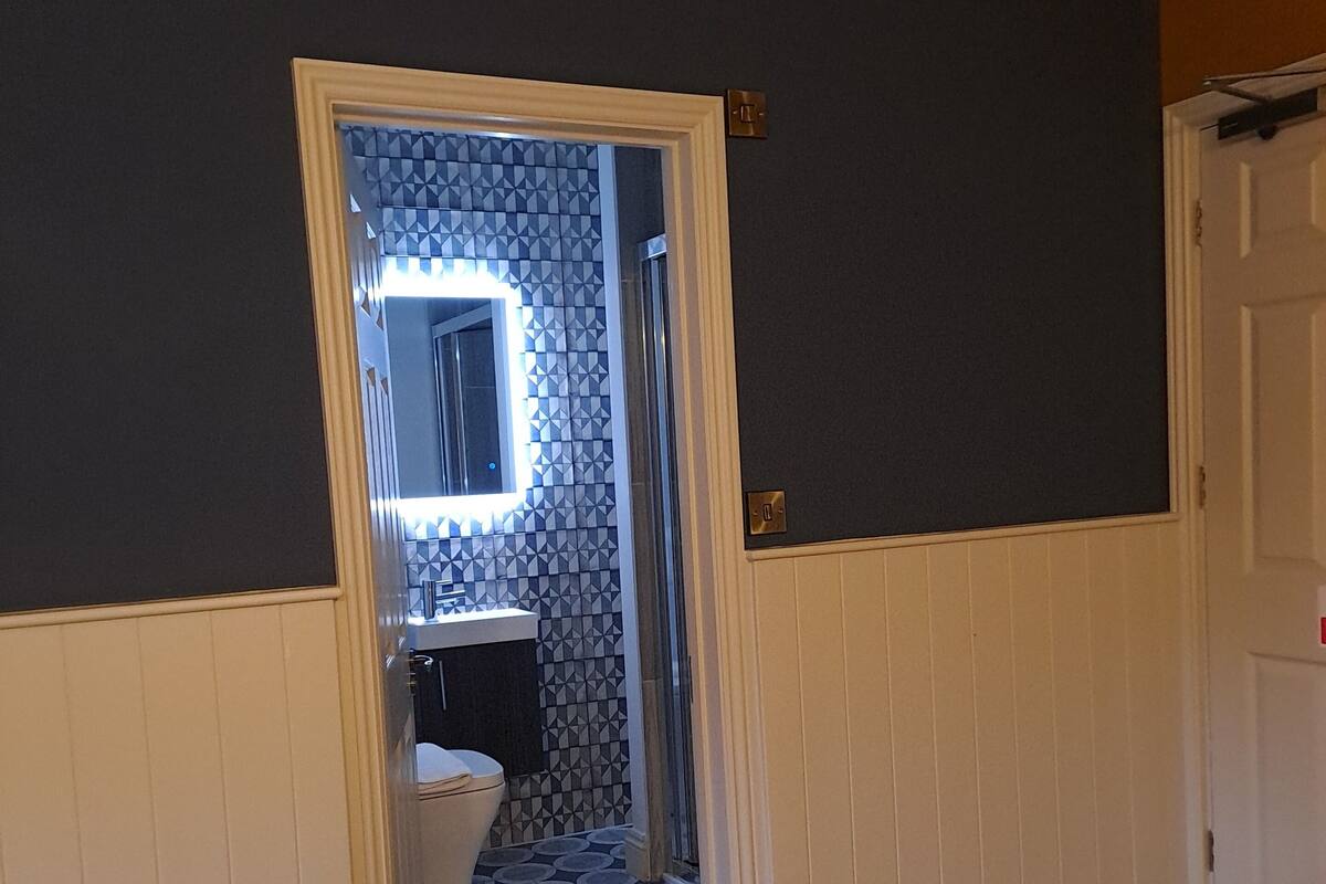 A hotel room with a bed, a bathroom visible through an open door, and a mirror with a geometric pattern on the wall.