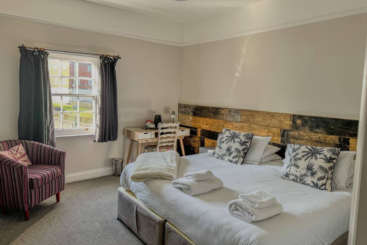 A bedroom with a bed, a desk, a chair, and a window with curtains.
