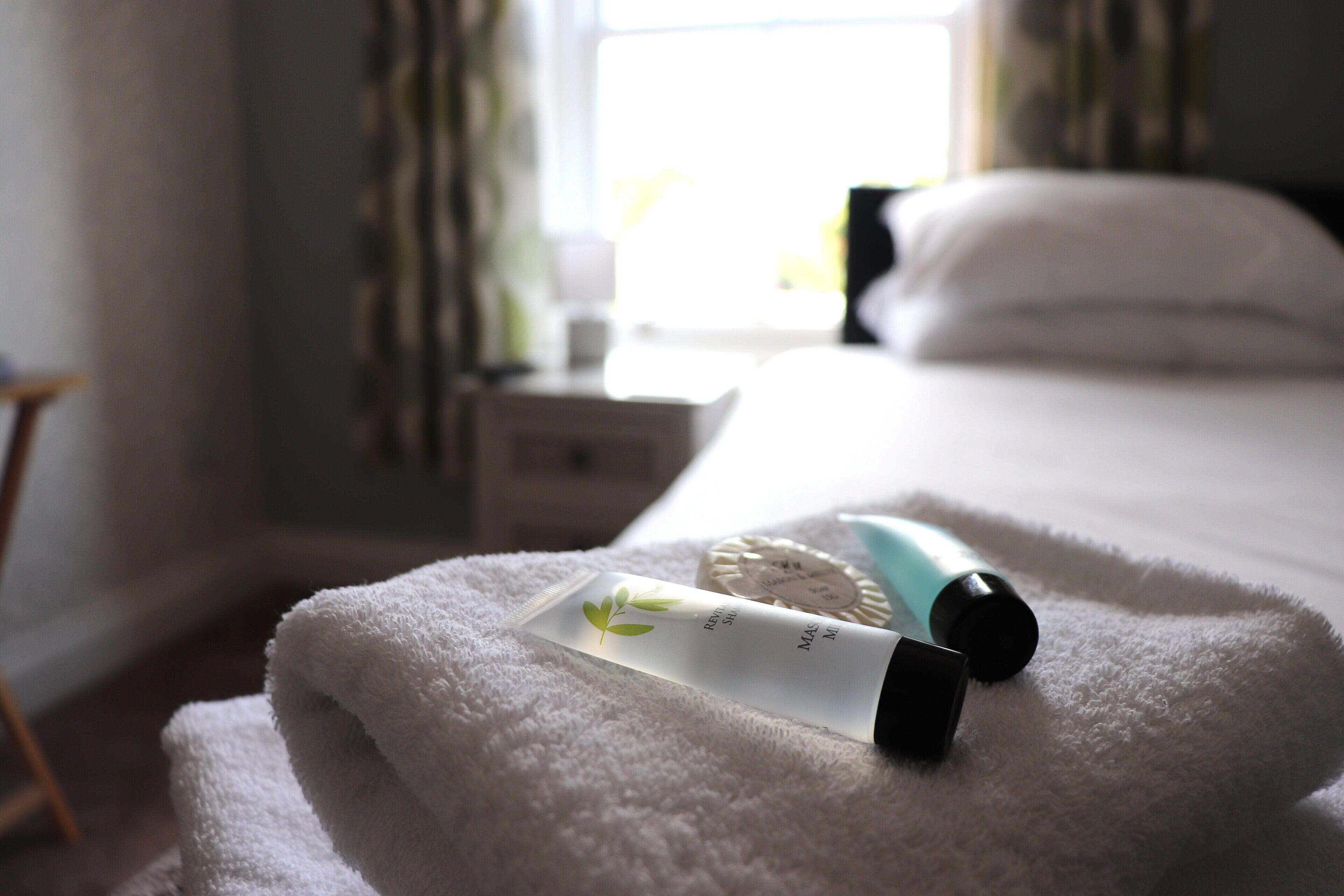 A neatly made bed with a white towel, a bottle of lotion, and a small container on the bed.
