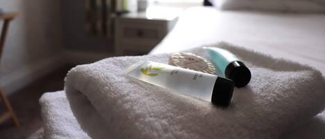 A neatly made bed with a white towel, a bottle of lotion, and a small container on the bed.