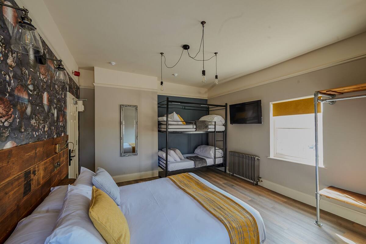 A bedroom with a large bed, a bunk bed, a wooden headboard, a chandelier, a radiator, and a window.