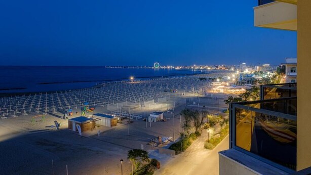 A beach with rows of umbrellas, a Ferris wheel, and a cityscape in the background.