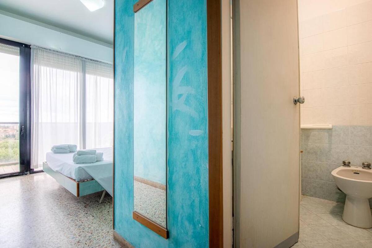 Habitación de hotel con cama, baño con lavabo y espejo, y vista de la ciudad por la ventana.
