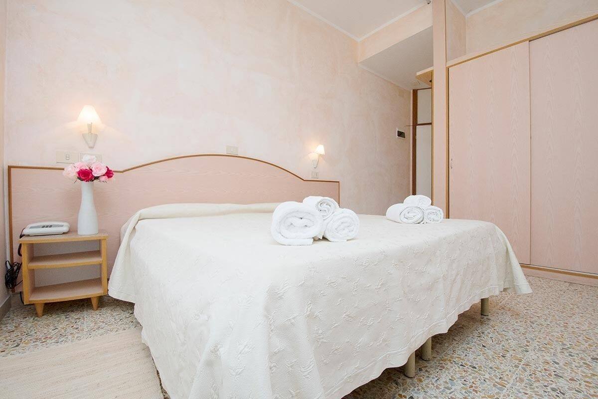 Habitación de hotel con cama, mesita de noche con lámpara y luz en la pared.