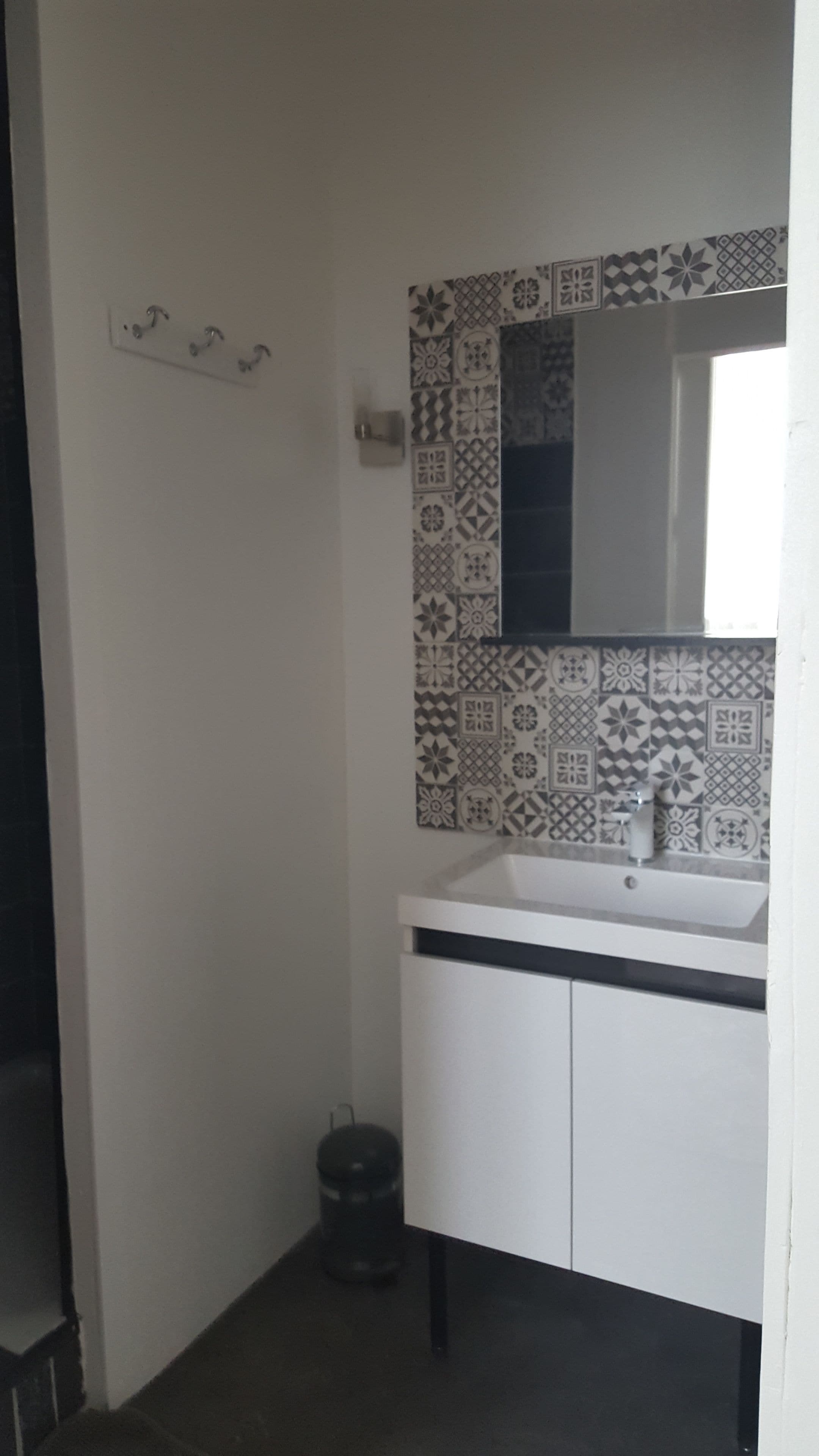 A bathroom with a white sink, a mirror, and patterned tiles on the wall.