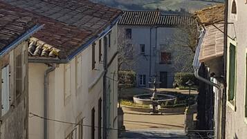 A narrow street flanked by buildings with traditional architecture, leading to a courtyard with a fountain.