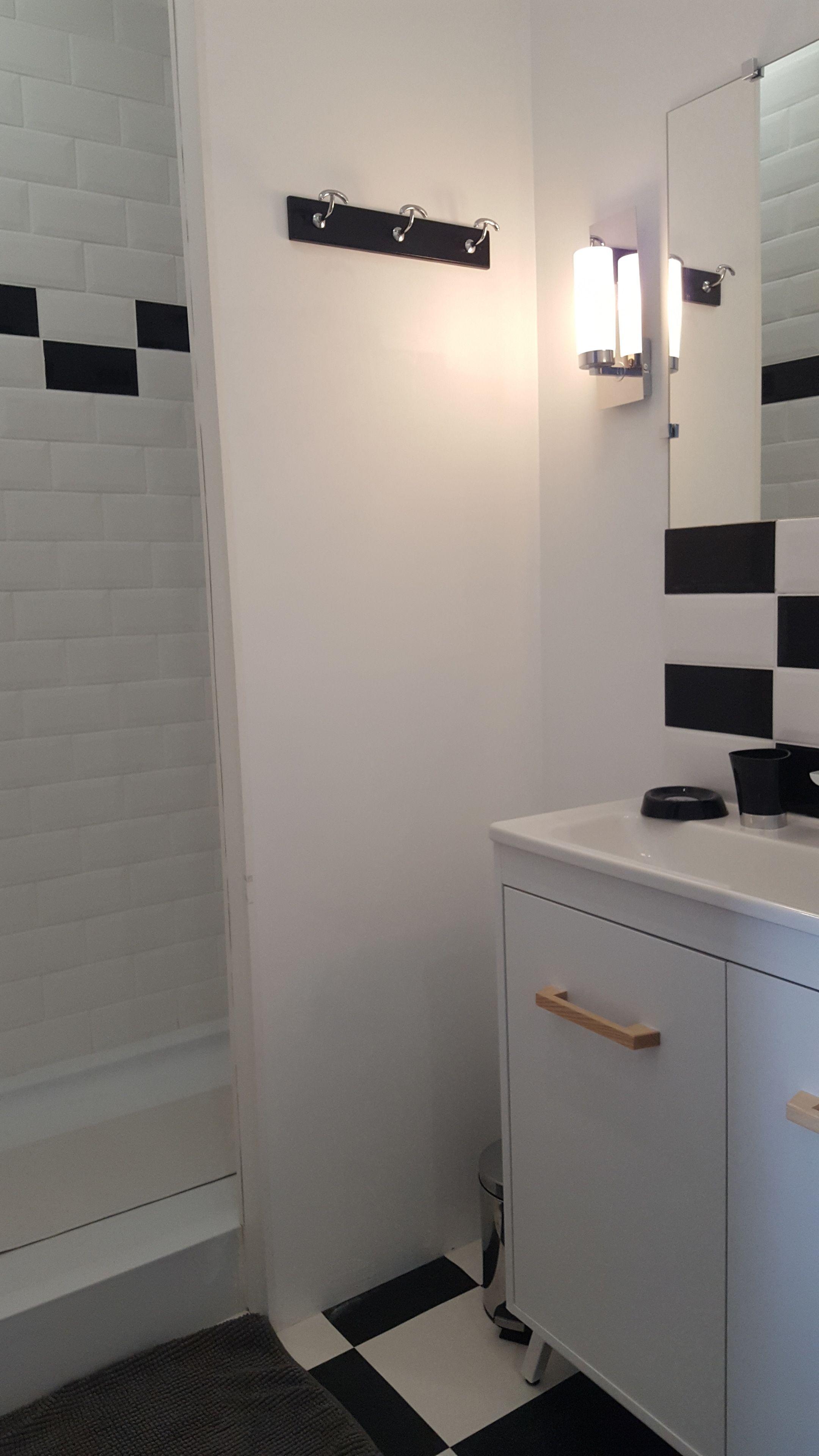 Un baño con un lavabo blanco, un espejo y un suelo a cuadros blanco y negro.