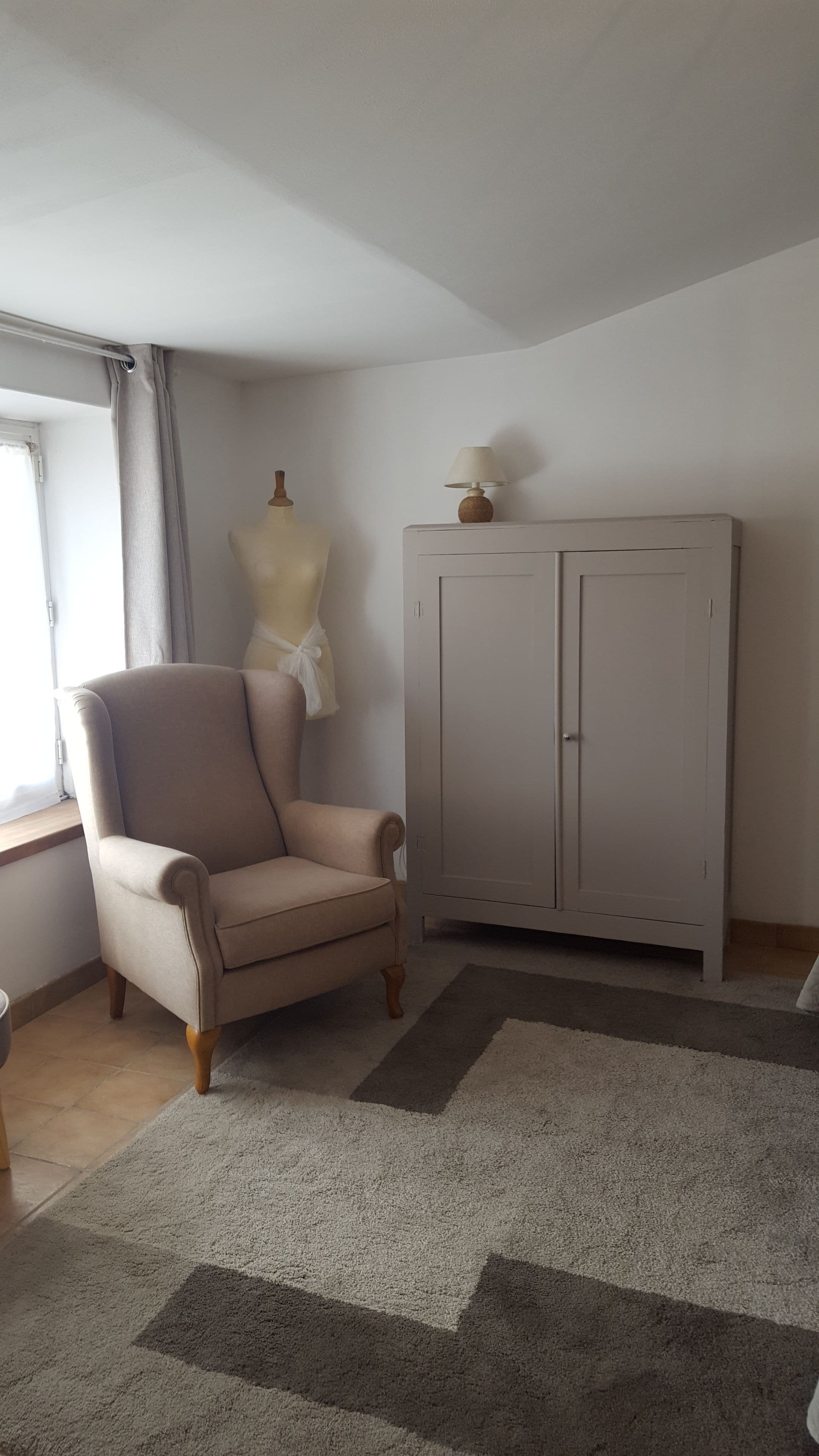 A room with a beige armchair, a wardrobe, and a mannequin dressed in white.