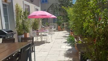 Un patio al aire libre con mesas, sillas, un paraguas rosa y una parrilla.