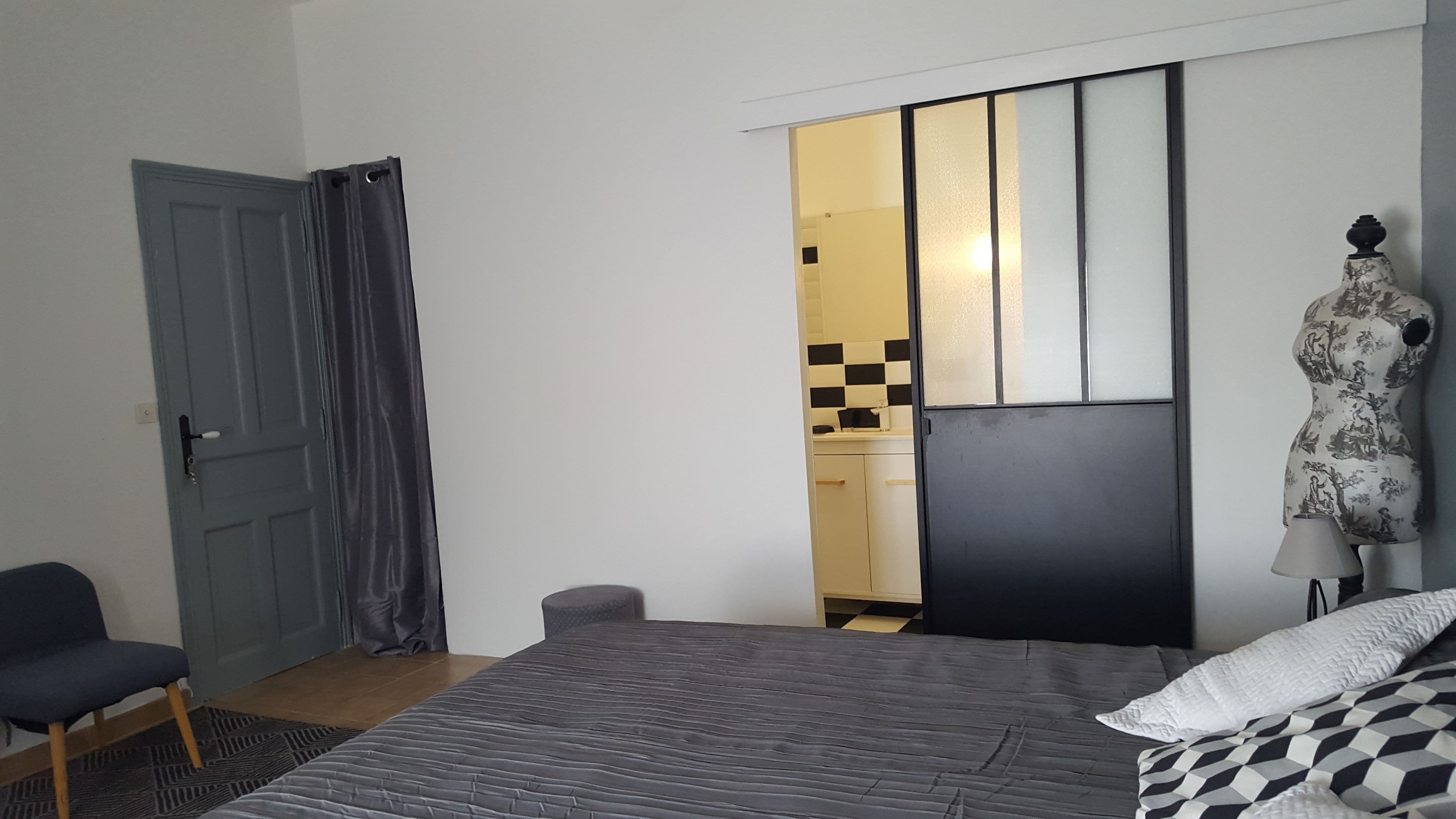 A bedroom with a bed, a chair, a wardrobe, and a bathroom visible through an open door.