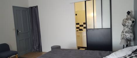 A bedroom with a bed, a chair, a wardrobe, and a bathroom visible through an open door.