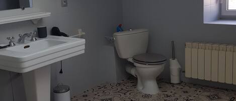Baño con lavamanos, inodoro y radiador. El suelo tiene baldosas estampadas.