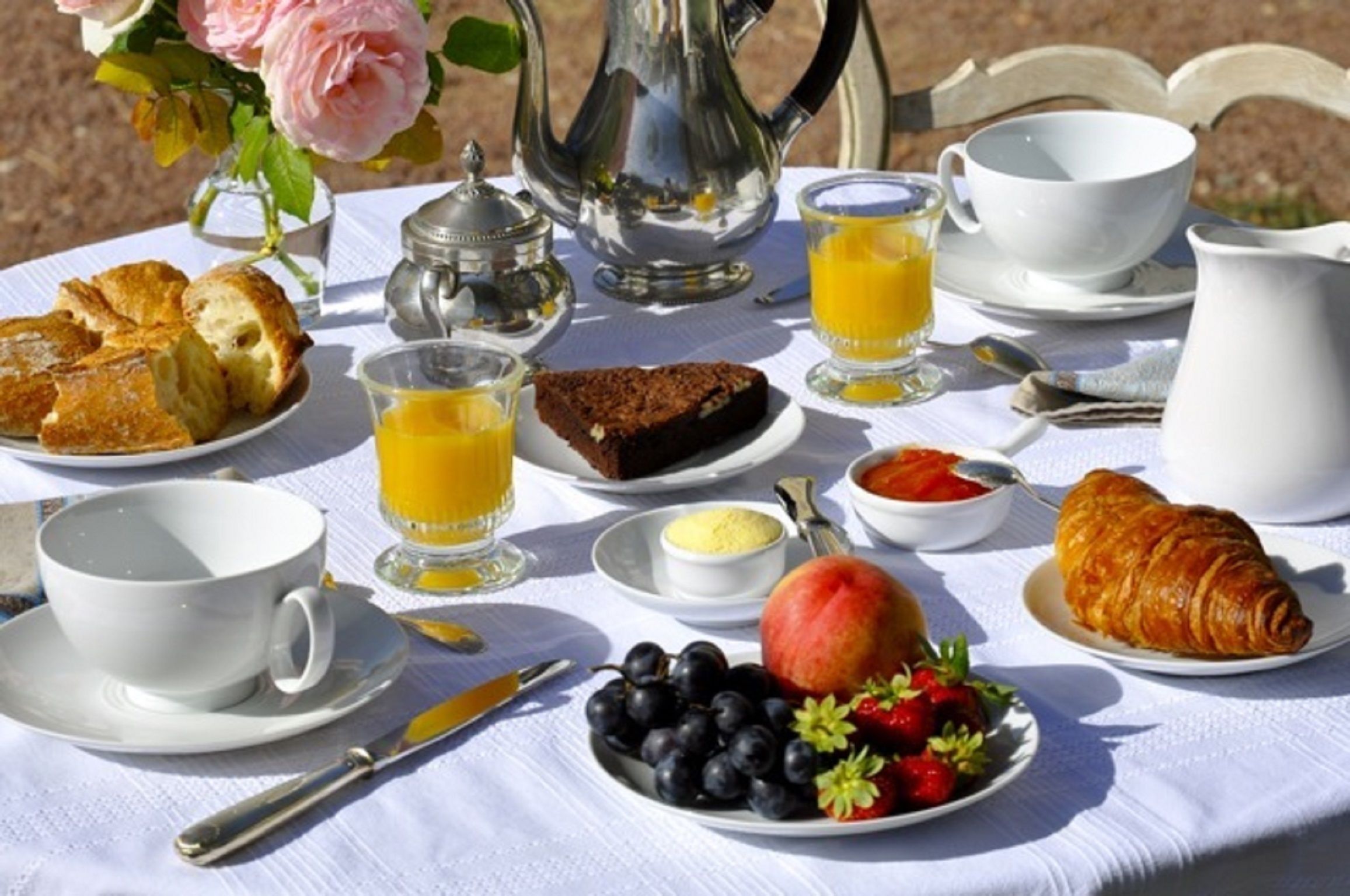 Una mesa de desayuno con croissants, fruta, jugo y café.