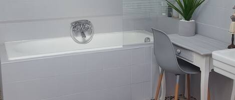 A bathroom with a bathtub, a sink, a chair, and a potted plant.
