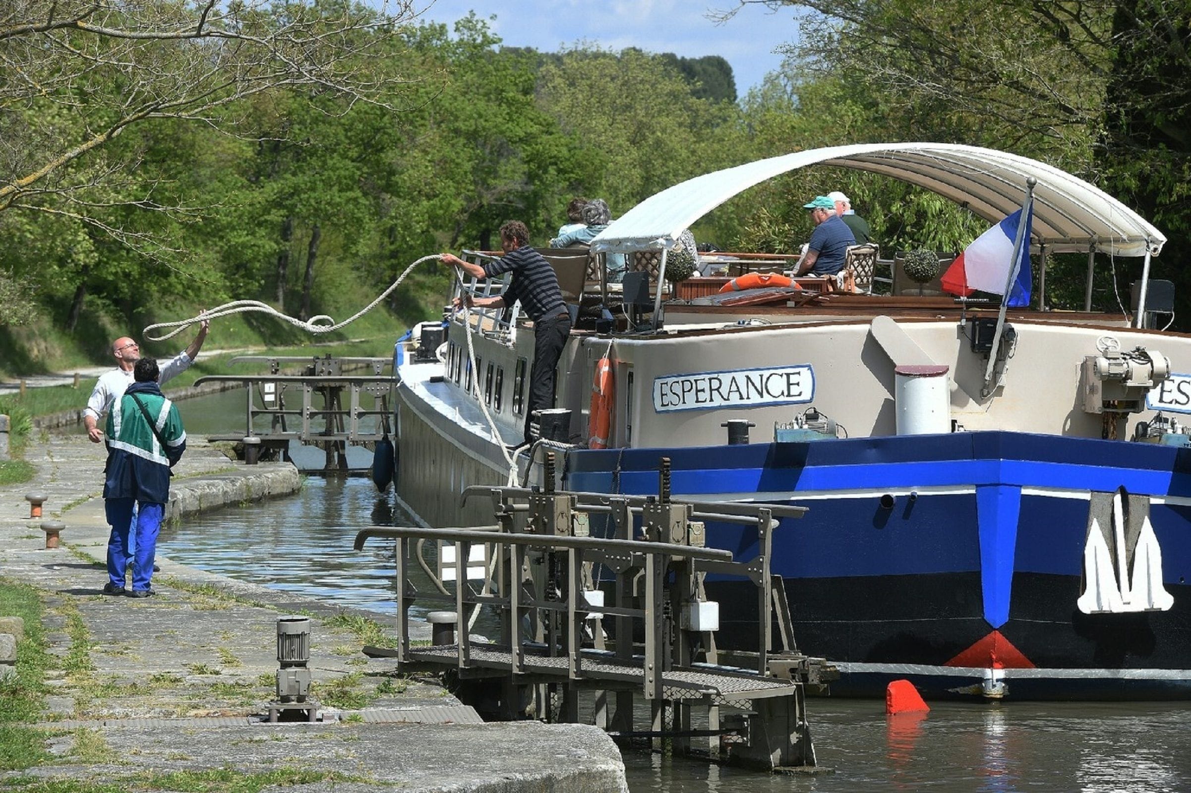 A boat docked at a lock system with people on board and a person standing on the dock.