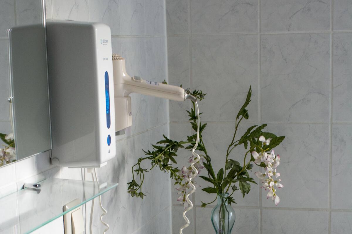 A bathroom with a white sink, a mirror, a glass vase with flowers, and a toothbrush holder.