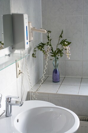 A bathroom with a white sink, a mirror, a glass vase with flowers, and a toothbrush holder. - Altes Bierhaus Landhotel (Arzbach)