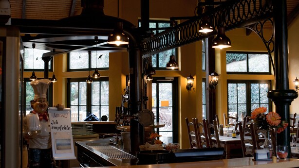 Interior de restaurante con techo alto, vigas a la vista y ventanas amplias.