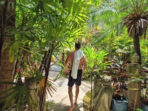 A man walking through a lush garden with dense foliage and a statue.