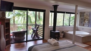 A bedroom with a large window, a wooden floor, a bed, a black stove, a sink, and a view of palm trees. - Alaya Ascend  |  Legian Executive Pool-view Room |  Sunshine Coast Retreat (Eudlo)