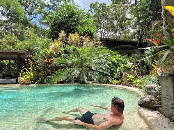 A man relaxing in a clear pool surrounded by lush tropical vegetation.