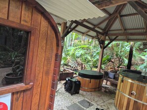 A wooden structure with a covered patio area, a hot tub, and various potted plants.