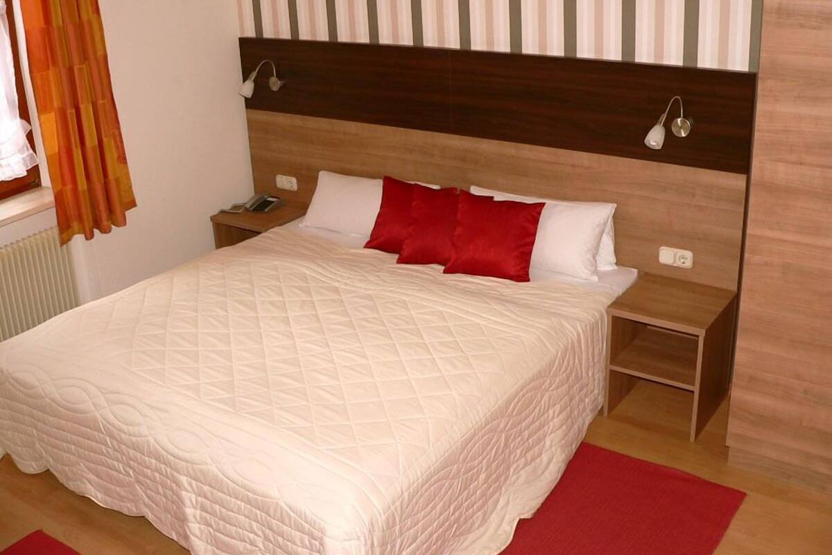 Un lit bien fait, recouvert d’une courtepointe matelassée, deux tables de chevet avec des lampes et une fenêtre avec des rideaux.