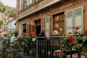 An outdoor café with wicker furniture and red flowers, set against a stone building with green shutters. - Fränkischer  Gasthof  Hotel Zum Koppen (Gemuenden)