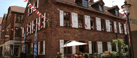 A traditional European building with a brick facade, multiple windows with shutters, and a small outdoor seating area with tables and chairs.