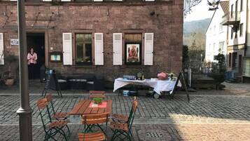 Ein Sitzbereich im Freien mit Tisch und Stühlen, eine Wandmalerei am Gebäude und eine Treppe, die zu einer oberen Ebene führt.
