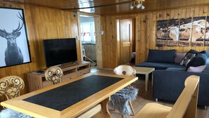 A wooden interior with a dining table, sofa, and television.