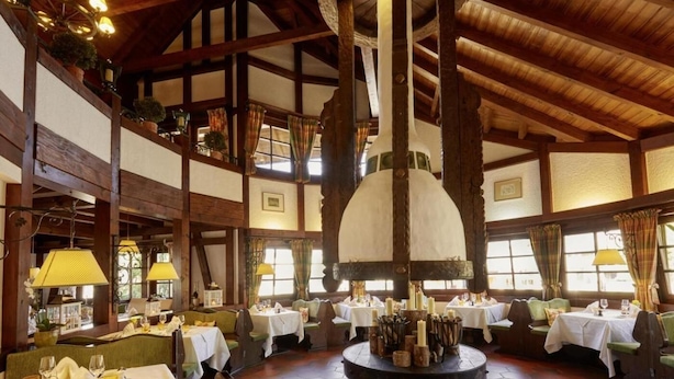 A restaurant with wooden beams, round tables, and a central chandelier.