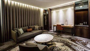 A modern hotel room with a sofa, a round coffee table, a desk, and a kitchen area. - JSL Hotel (Taipei)