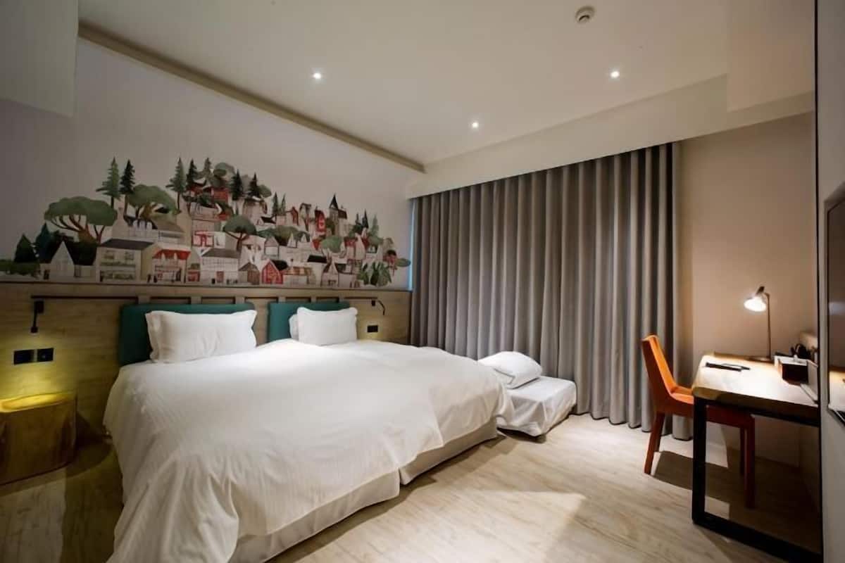 A hotel room with a bed, a desk, a chair, and a large window with curtains.