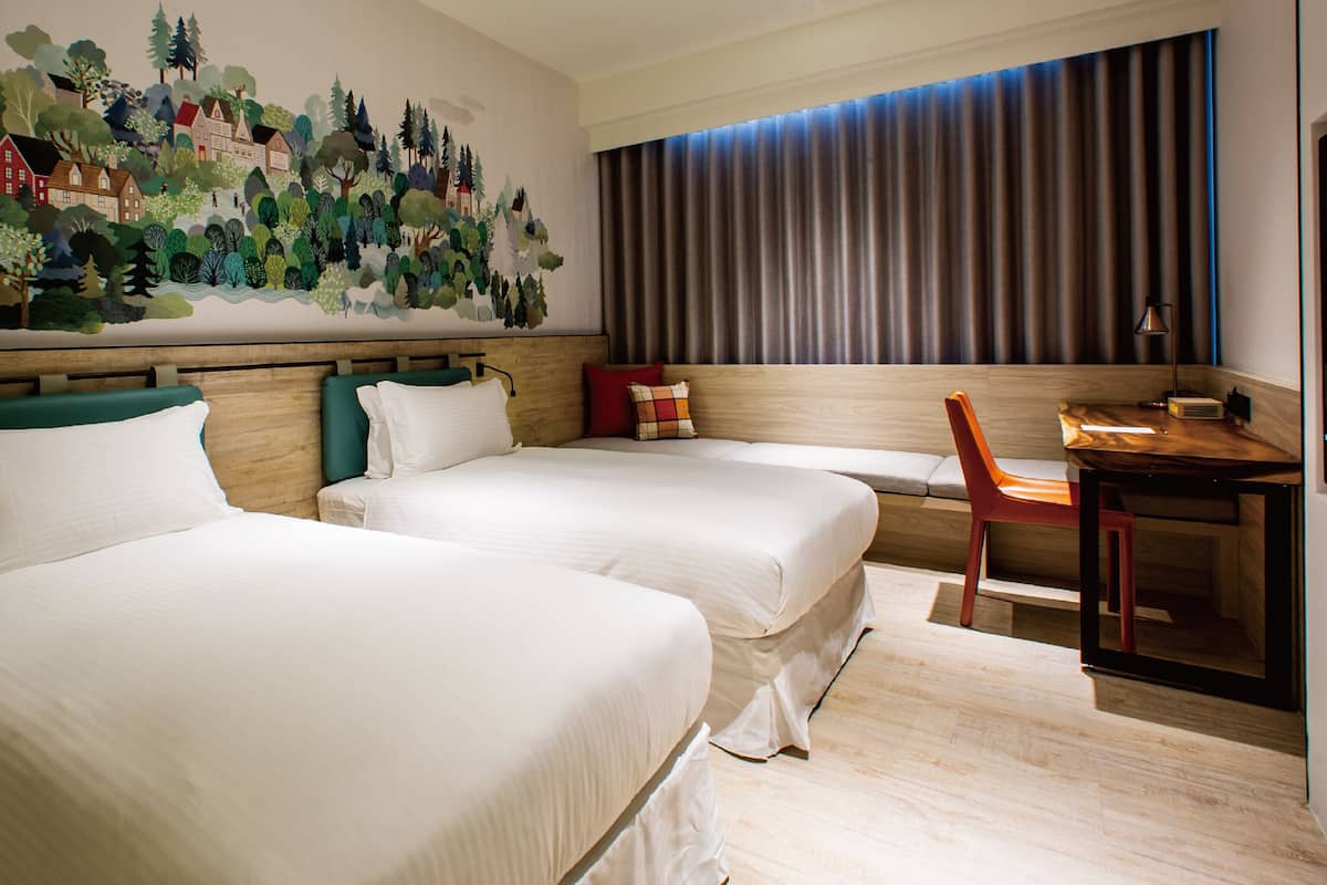 A hotel room with two beds, a desk, and a large mural on the wall.