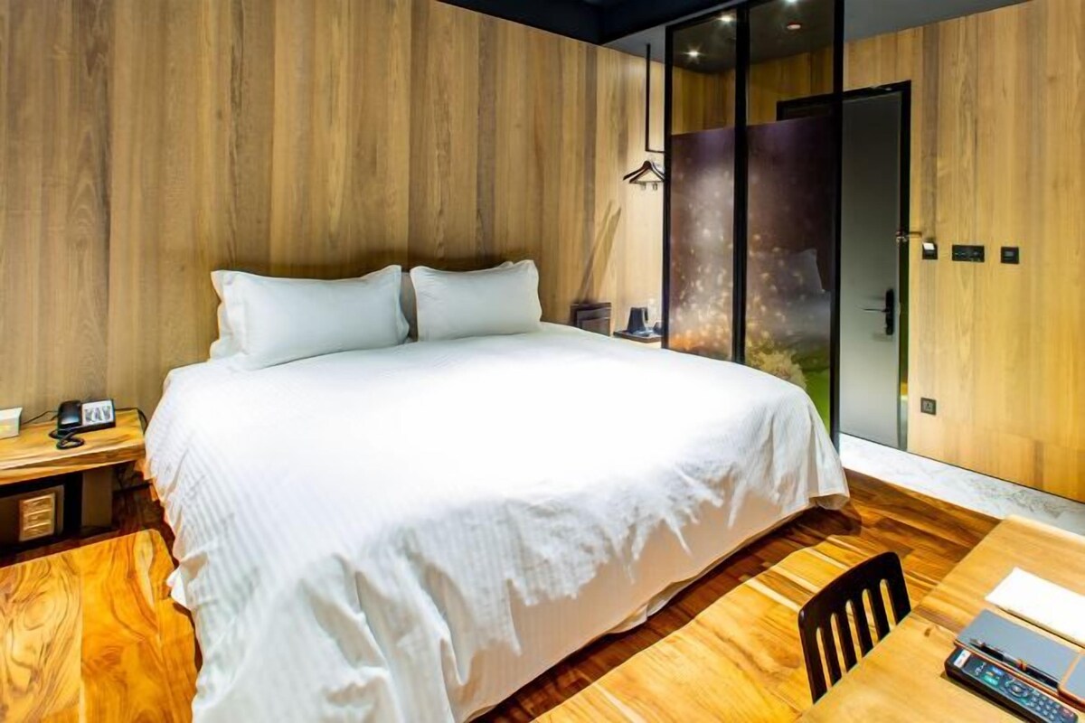 Un dormitorio moderno con una cama grande, suelo de madera, un escritorio con silla y un ventanal corredero que da a un balcón.