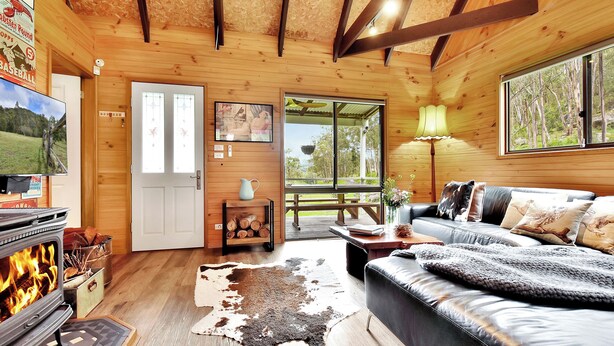 L’intérieur chaleureux d’un chalet avec une cheminée, un canapé en cuir et une grande fenêtre donnant sur le paysage extérieur.